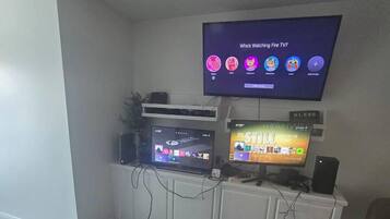Un salon avec un téléviseur à écran plat fixé au mur, une console de jeux et un canapé.