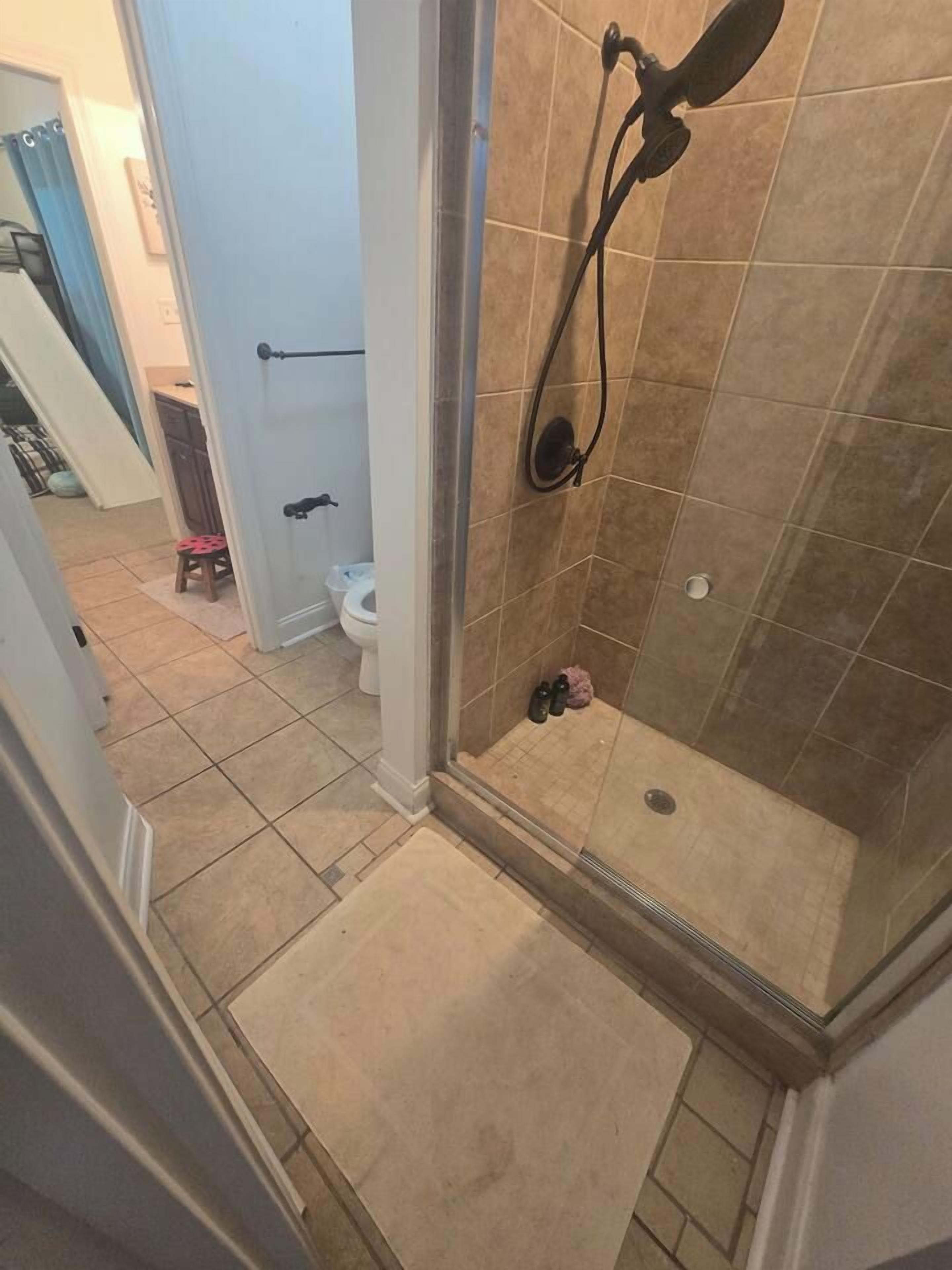A shower with a glass door, a toilet, and a small stool in the background.