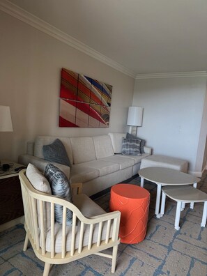 Una sala de estar con un sofá, una silla de madera, una mesita y un otoman rojo.