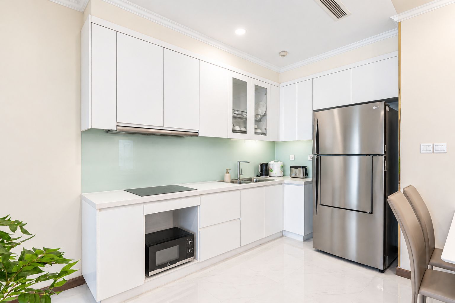 A modern kitchen with white cabinetry, a stainless steel refrigerator, a microwave, and a sink.