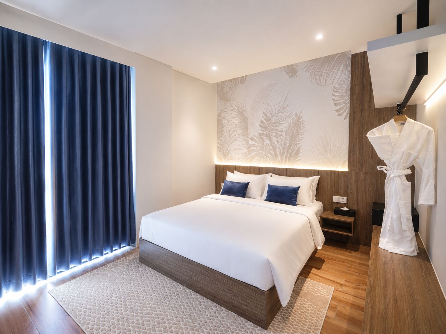 A modern hotel room with a large bed, a robe hanging on the wall, and a patterned wall design.