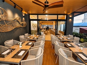 A restaurant with wicker furniture, wooden tables, and a ceiling fan. - One Studio Suite (Poipet)
