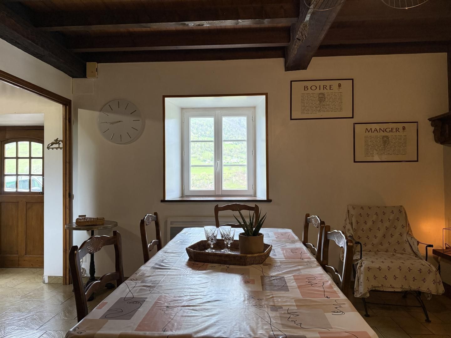 A dining area with a table set for two, a clock, and framed informational posters on the wall.
