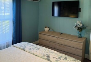Ein Schlafzimmer mit einem Bett, einem Schminktisch, einem flachbildfernseher an der Wand und einem Fenster mit Vorhängen.