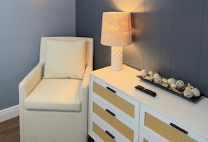 Ein Zimmer mit einem weißen Sessel, einem weißen Beistelltisch mit einer Lampe und Dekoelementen.