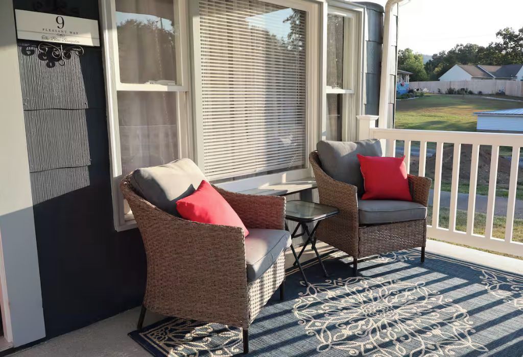 Eine Veranda mit Korbmöbeln, einem kleinen Tisch und Blick auf einen Garten.