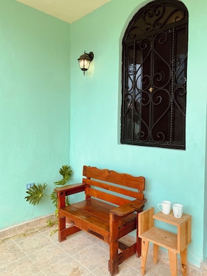 A wooden bench with a small table beside it, a wall-mounted light, and a decorative window. - Minutes to Tourist Attractions, Hospital Zone, Airport, ADO, Stores, Restaurants (Mérida)