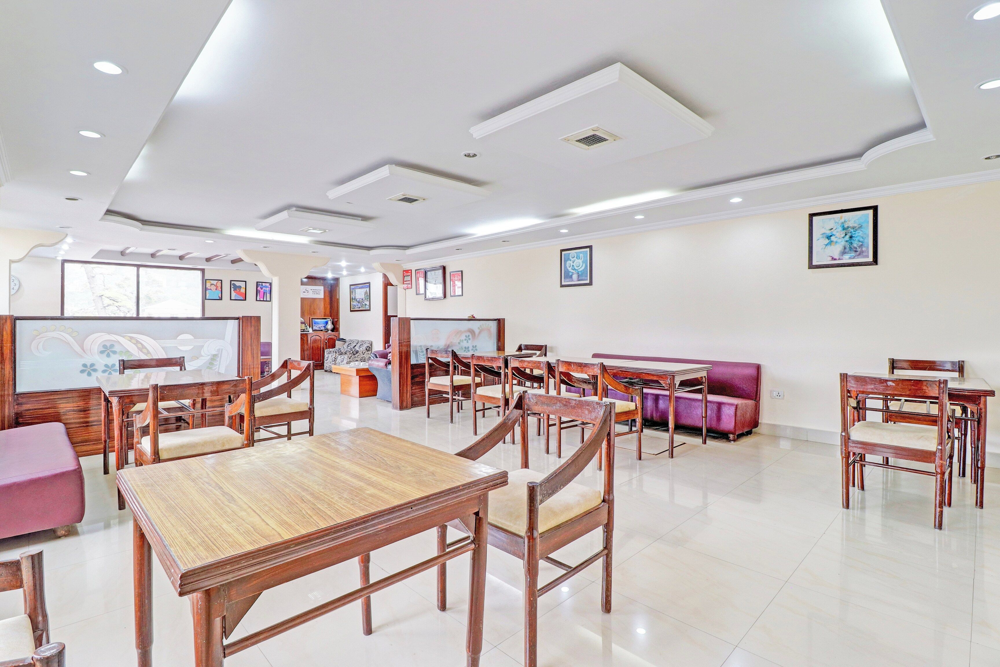 A spacious dining area with wooden tables and chairs, a sofa, and wall-mounted artwork.