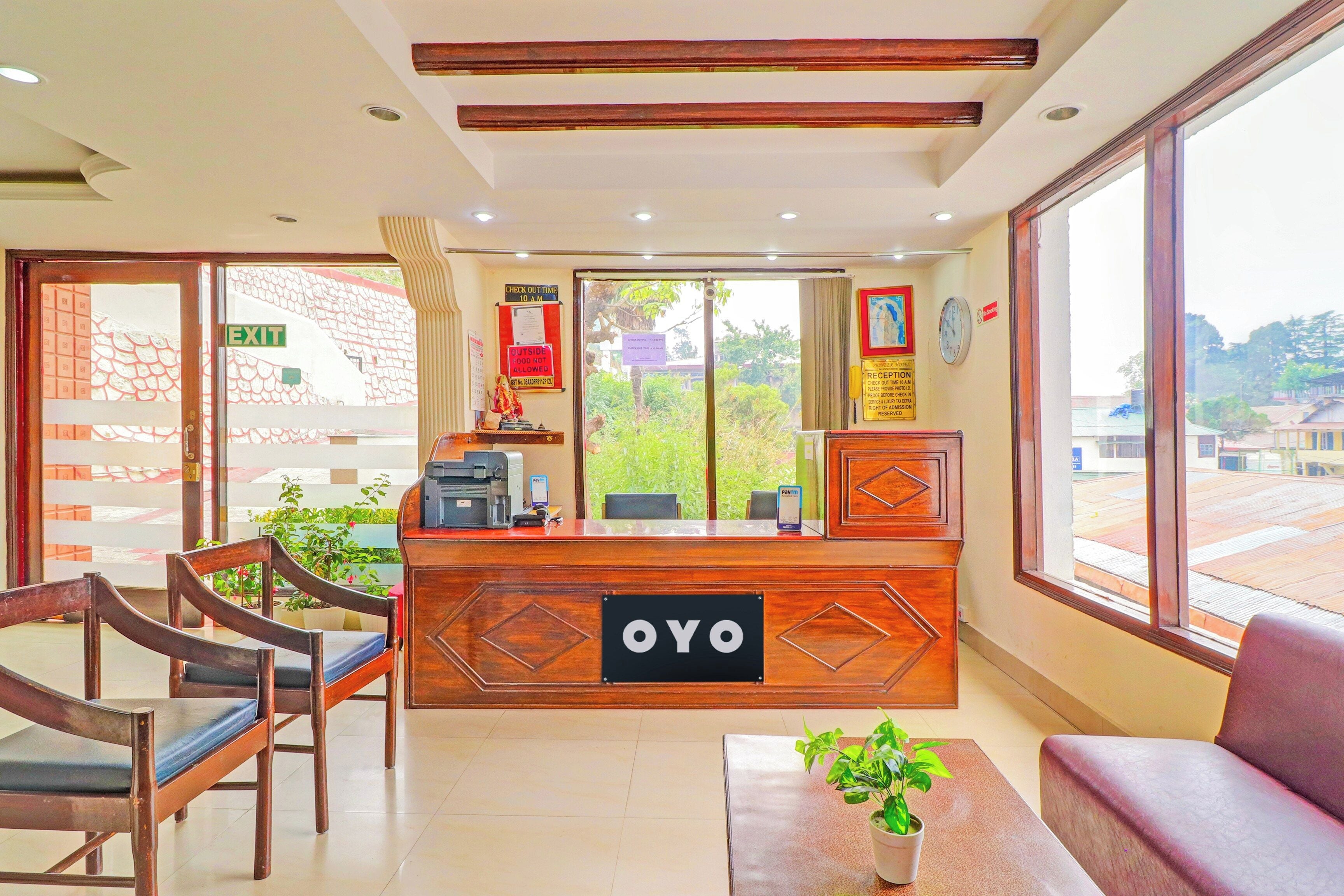 A reception area with a wooden reception desk, chairs, a potted plant, and a view of the outside.