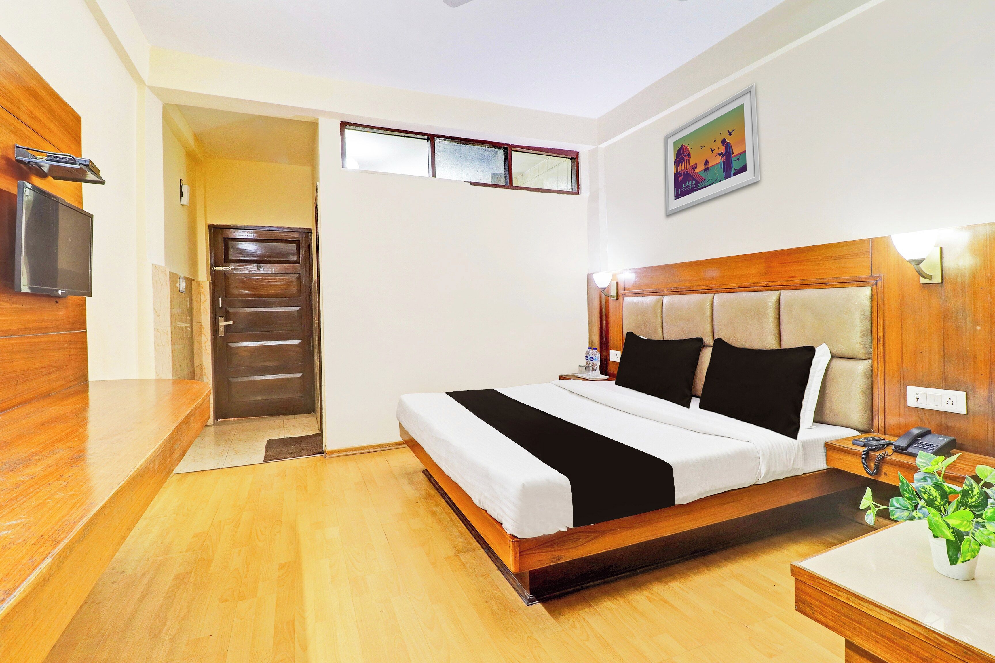 A hotel room with a wooden bed, bedside table, and a television.