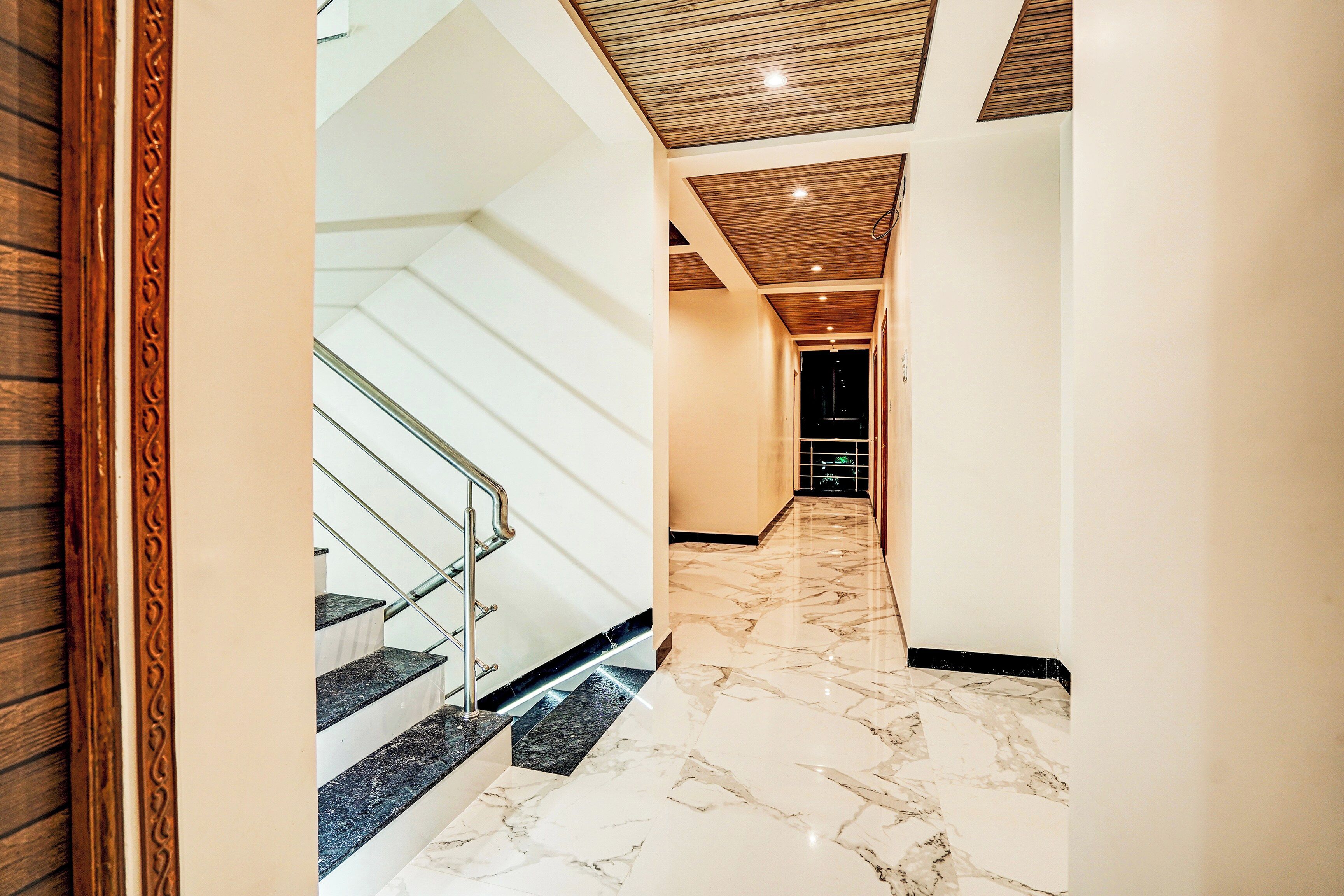 Un pasillo con piso de mármol, una escalera con barandillas de metal y paneles de techo de madera.