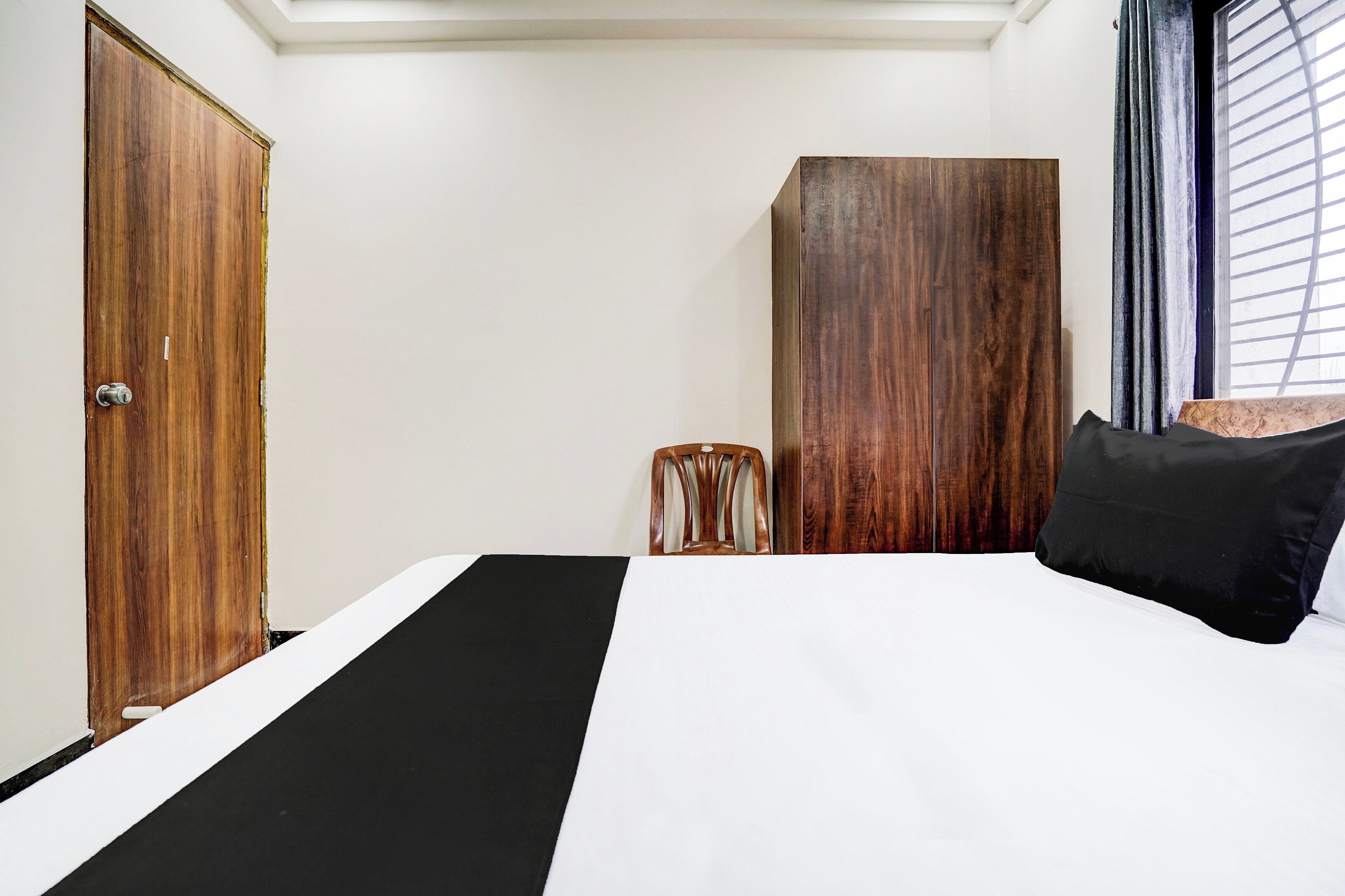 Ein Schlafzimmer mit einem Bett, einem Kleiderschrank, einem Sessel und einem Fenster mit Jalousien.