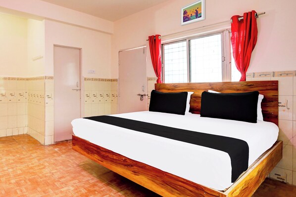 A hotel room with a wooden bed, a window with red curtains, and a tiled wall with a picture above the window. - Hotel O Sukoon (Nagpur)