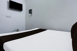 Habitación de hotel con cama, televisor de pantalla plana en la pared, toma de corriente y una mesita con hervidor y botella.