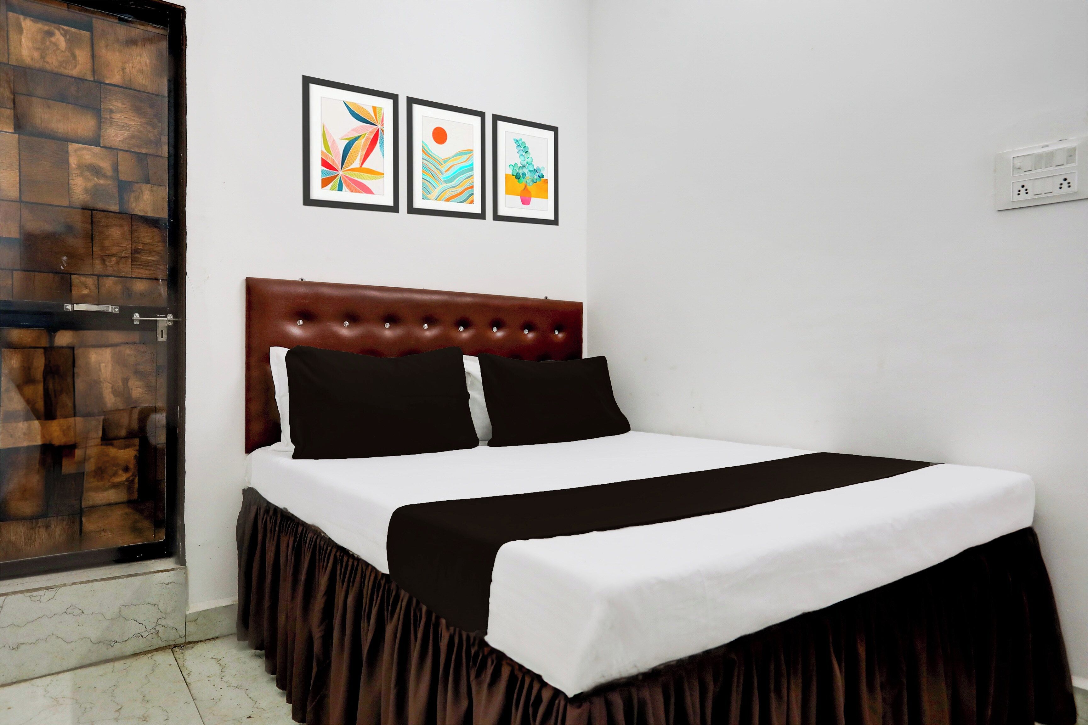 A bedroom with a bed, a wooden door, and three framed artworks on the wall.