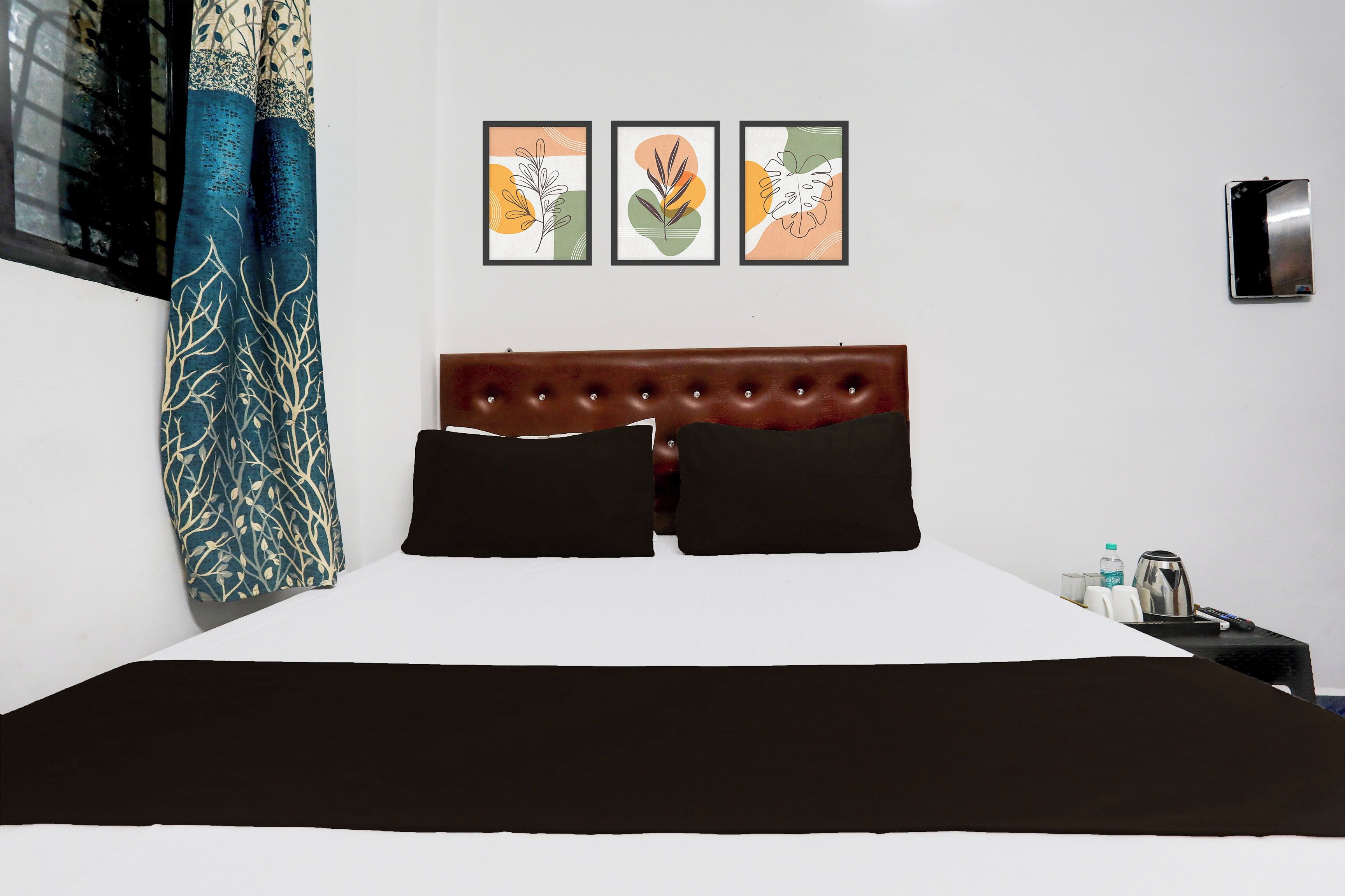 A hotel room with a large bed, a headboard, and three framed artworks on the wall.
