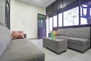 A modern waiting area with two sofas, a glass coffee table, and a door leading outside. - Hotel O by OYO JANNAT (Nagpur)