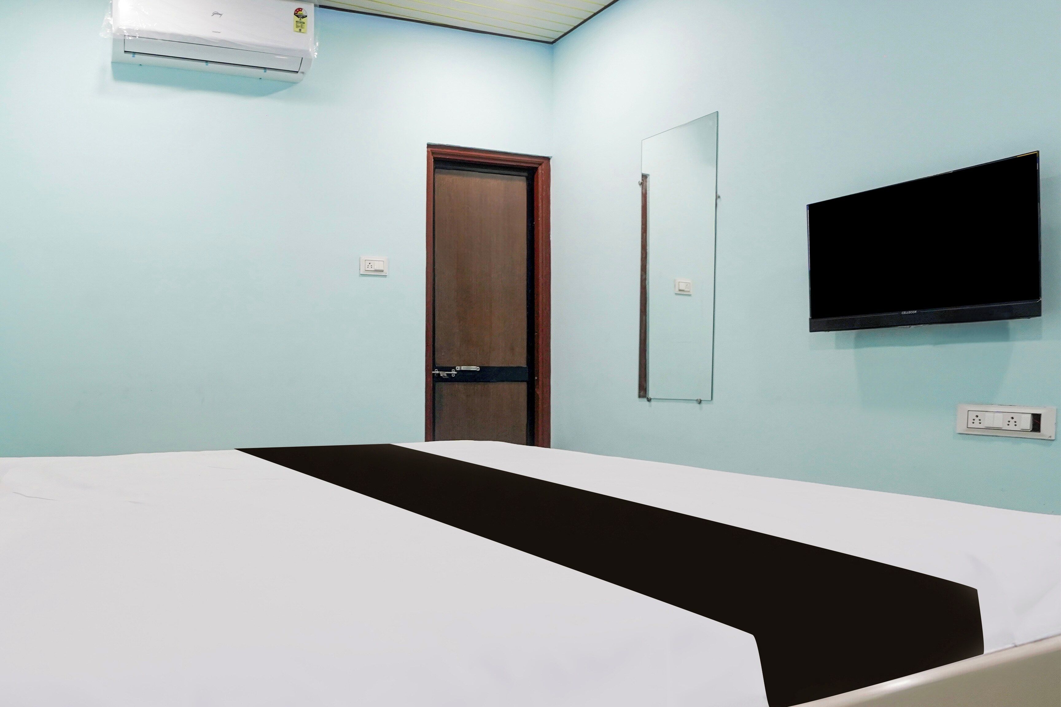 Quarto com cama, televisão fixada na parede e aparelho de ar condicionado.