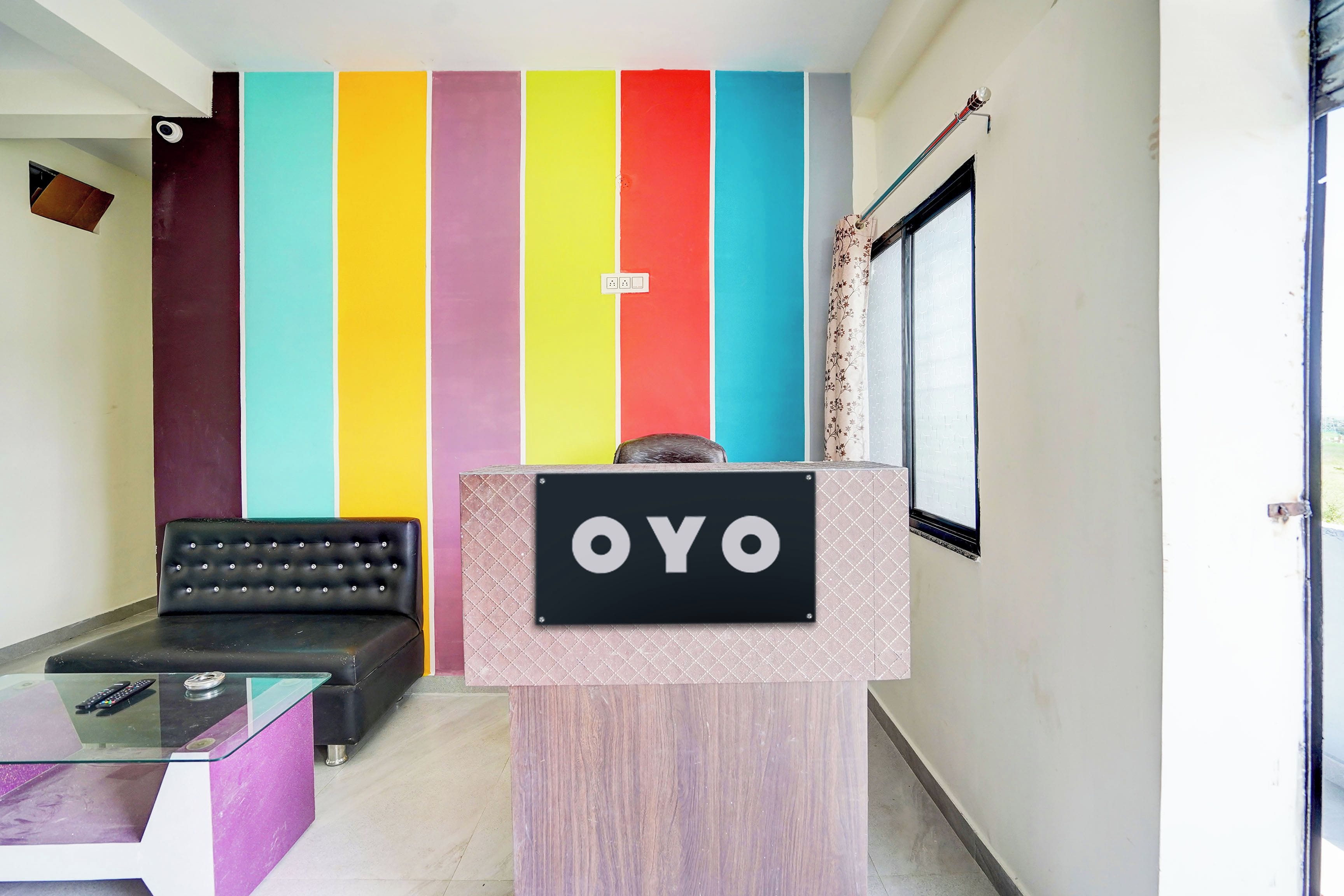 A reception area with a colorful wall, a black leather sofa, a glass table, and a sign that reads 'OYO'.