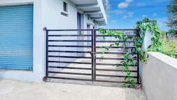 Une entrée fermée par un portail menant à un bâtiment doté d’une porte à volets bleus et d’une grille métallique.