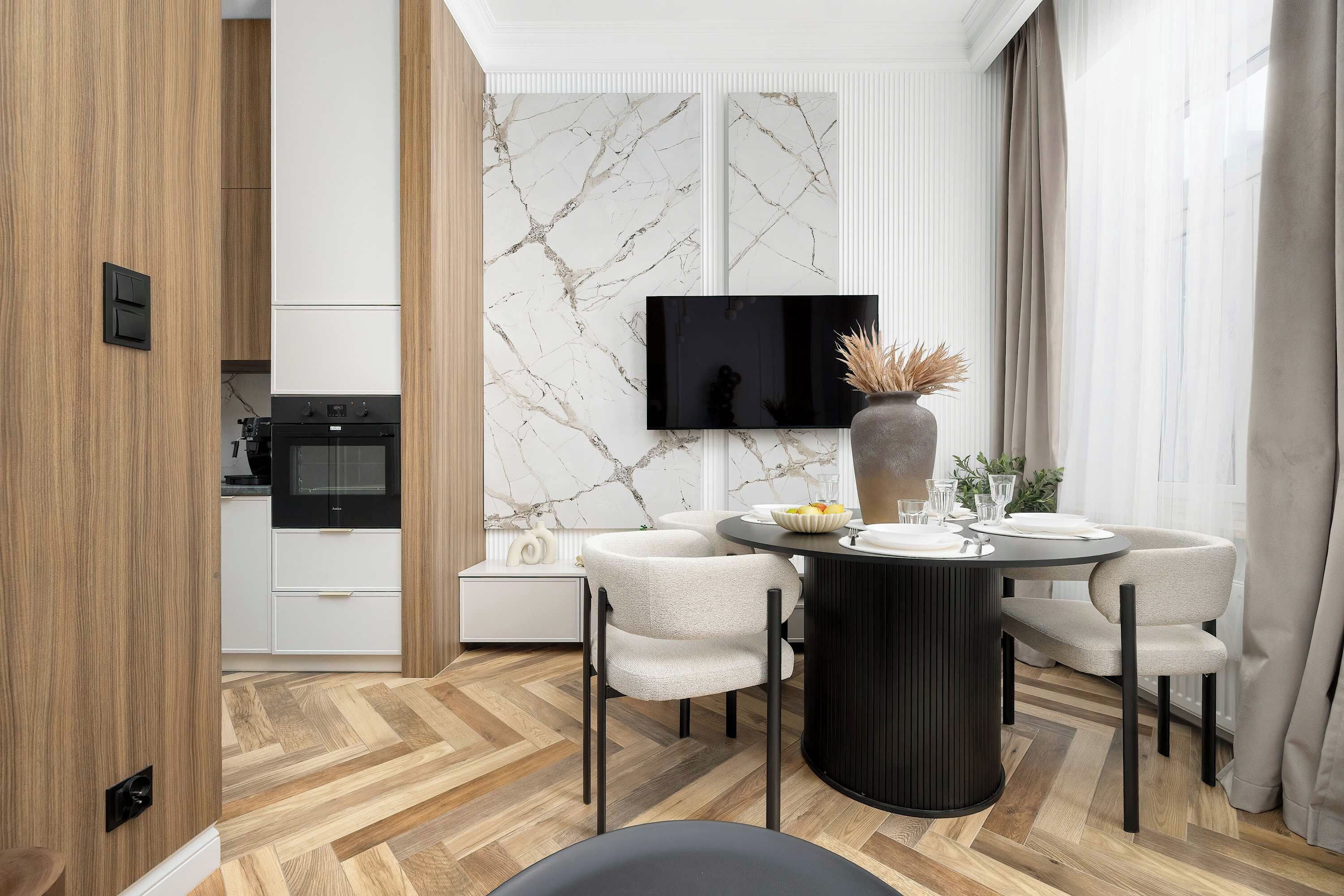 A modern dining area with a round table, four chairs, and a flat-screen TV mounted on the wall.