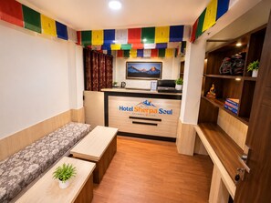 A hotel reception area with a sofa, a desk, a computer, and a shelf with helmets and books. - Hotel Sherpa Soul (Kathmandu)