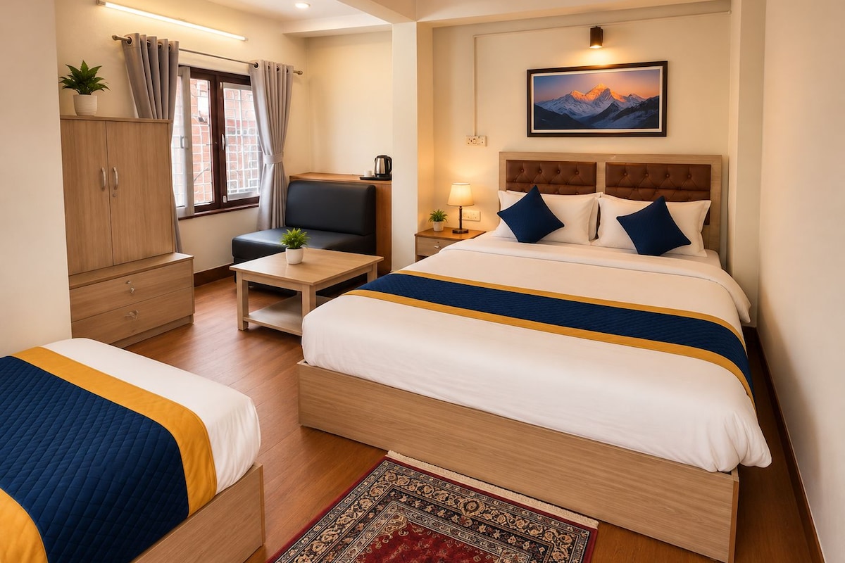 A hotel room with two beds, a sofa, a desk, a wardrobe, a ceiling fan, and a painting on the wall.