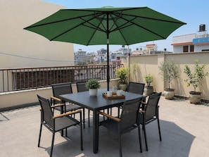 A rooftop terrace with a table and chairs, a green umbrella, and potted plants. - Hotel Sherpa Soul (Kathmandu)