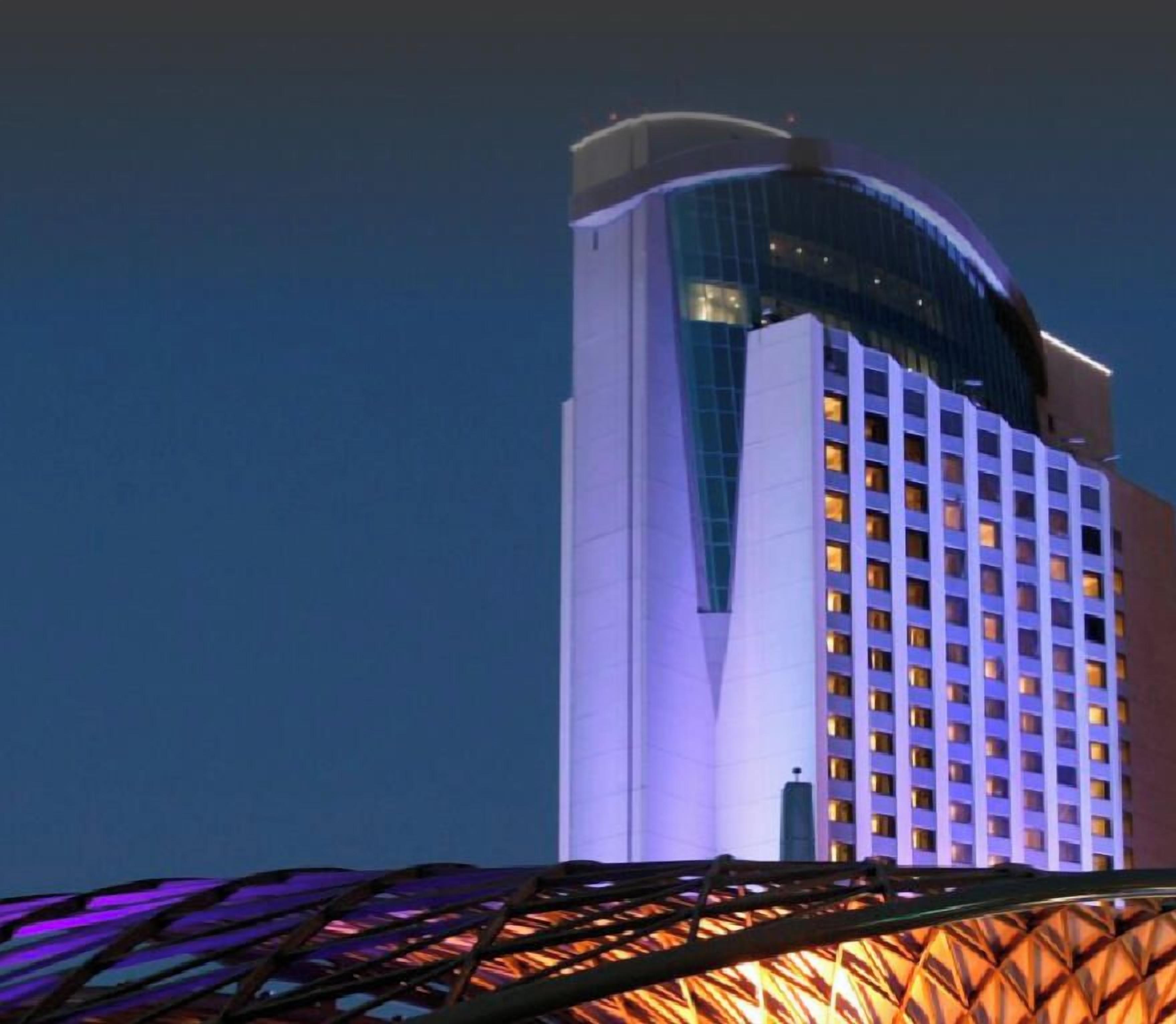 A high-rise hotel with a distinctive curved glass facade and a series of illuminated windows.