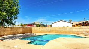 Una piscina residencial con un muro de ladrillo y un cielo azul despejado.