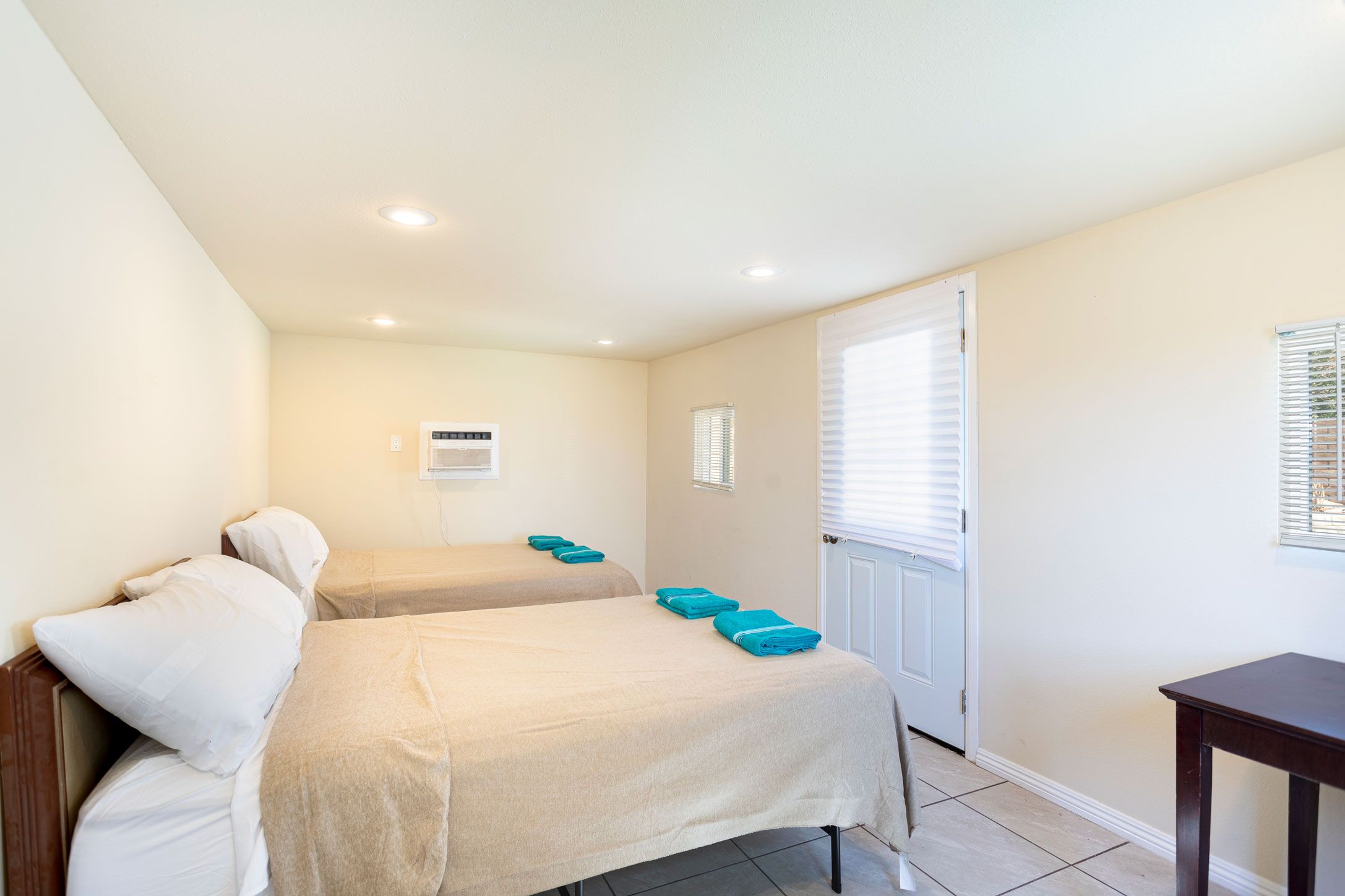 A hotel room with two beds, a small table, and a door with a window.