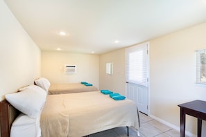 Habitación de hotel con dos camas, una mesita y una puerta con ventanal.