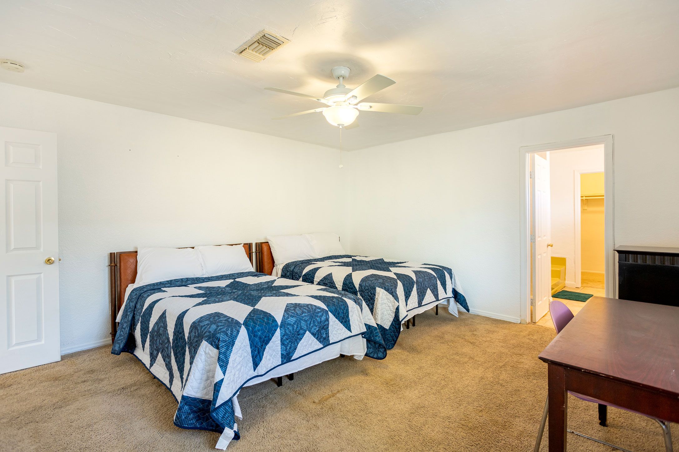 A bedroom with two beds, a ceiling fan, and a door leading to another room.