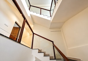 A modern interior with a staircase leading to an upper level, featuring glass railings and wooden handrails. - Austin Homes (Pallippuram)