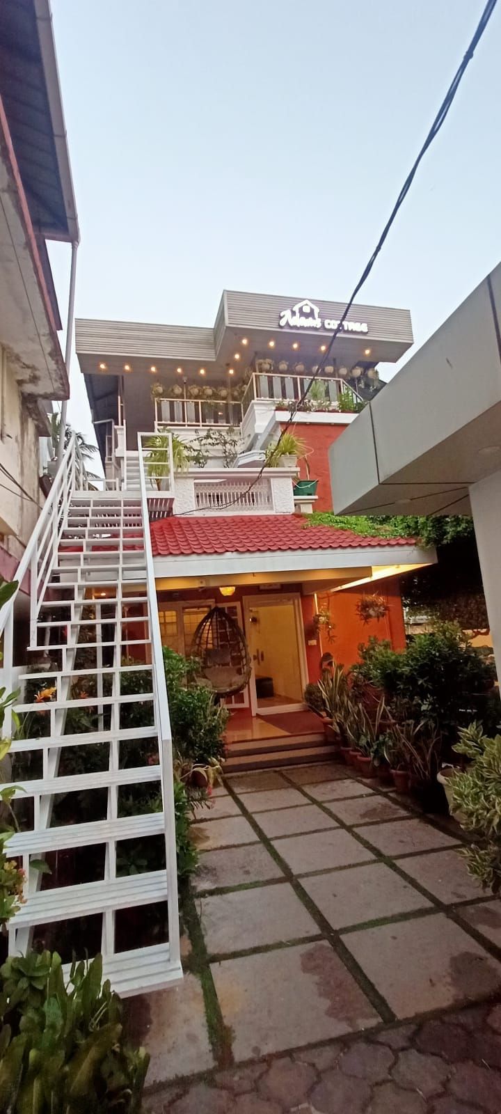 A hotel entrance with a staircase leading up to the main building, a red-tiled roof, and potted plants around the entrance.