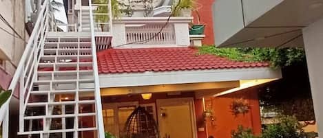 Entrada de un hotel con una escalera que conduce al edificio principal, techo de tejas rojas y plantas en macetas alrededor de la entrada.