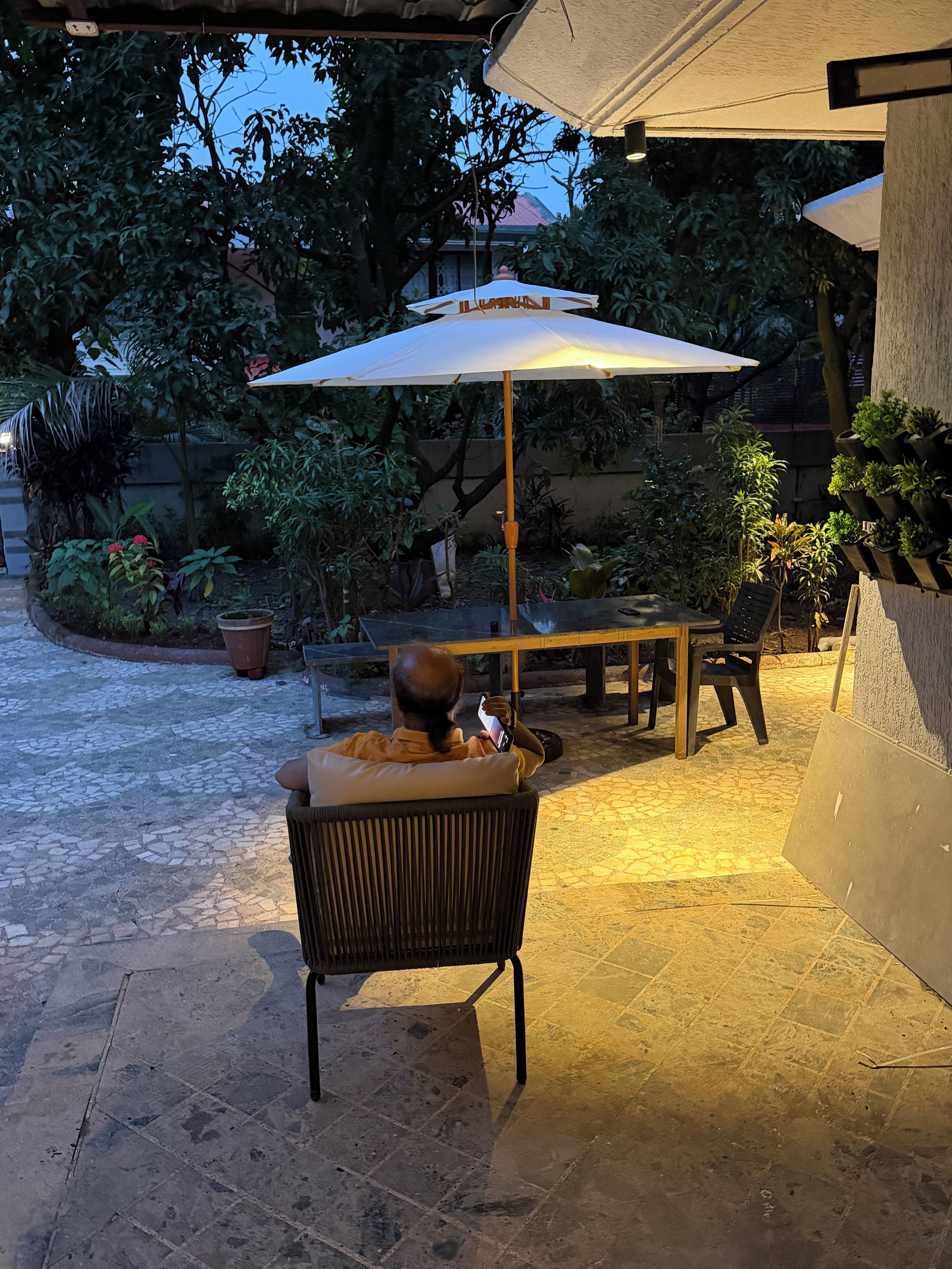 An outdoor patio area with a table and chairs, surrounded by potted plants and a large umbrella.
