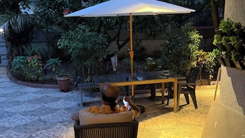 An outdoor patio area with a table and chairs, surrounded by potted plants and a large umbrella.