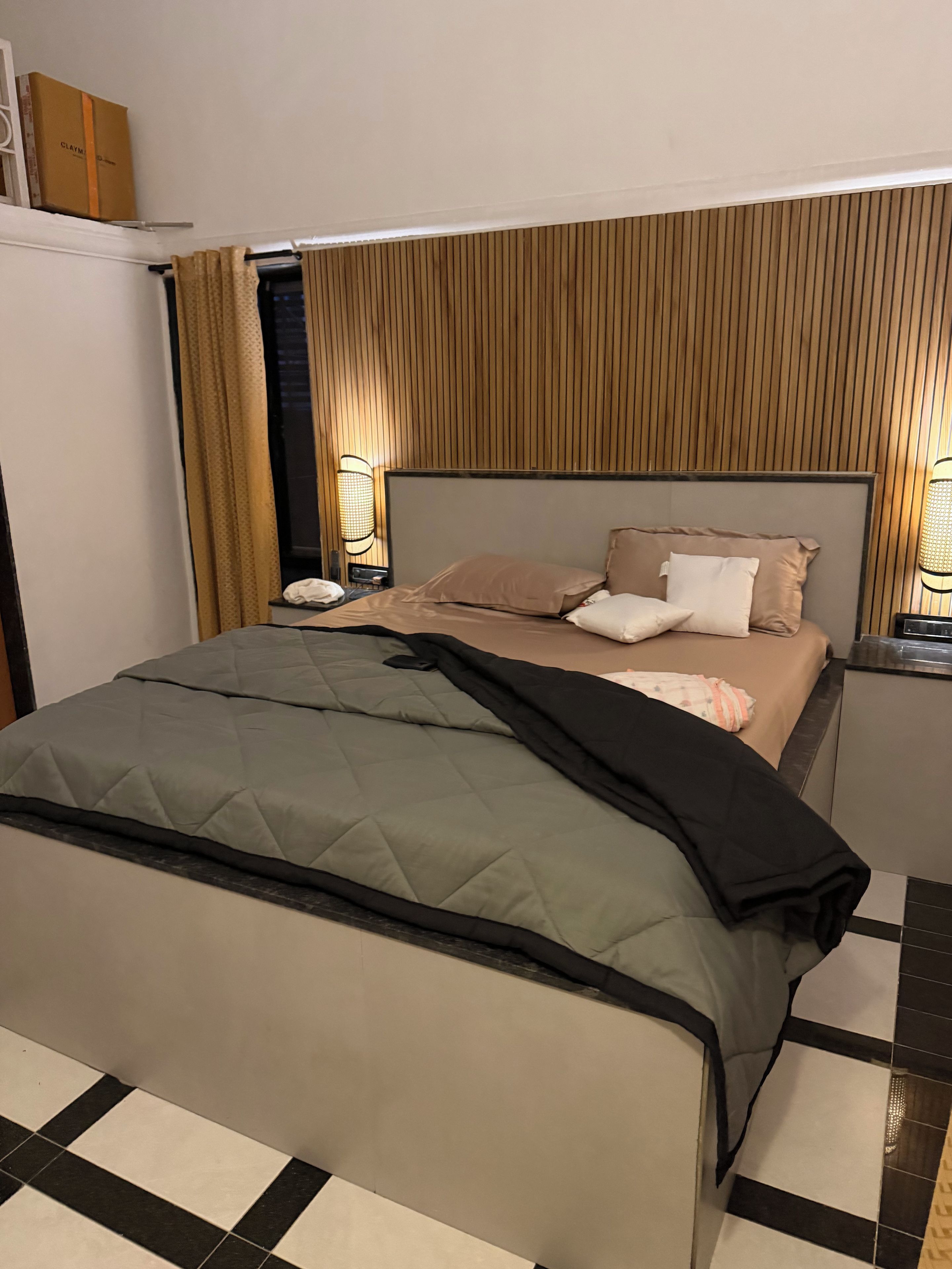 A hotel room with a bed, bedside tables, a nightstand, and a wall-mounted lamp.
