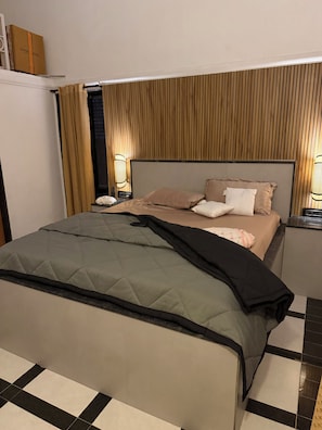 Hotellihuone, jossa on sänky, yöpöydät, yölamppu ja seinään kiinnitetty valaisin.