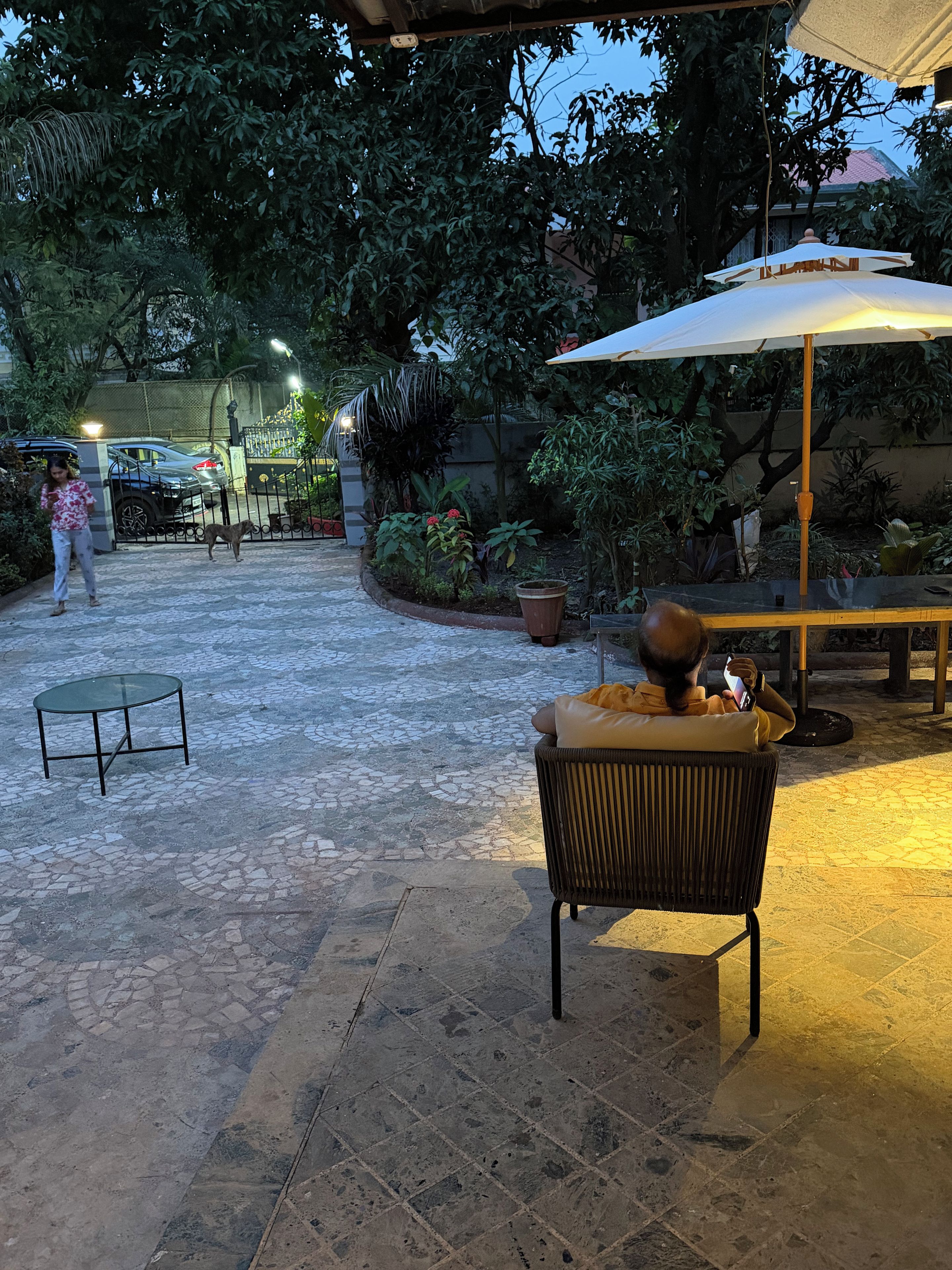 Un espace extérieur aménagé en terrasse, avec un sol carrelé, une chaise en osier, une table et un grand parasol pour créer de l’ombre.