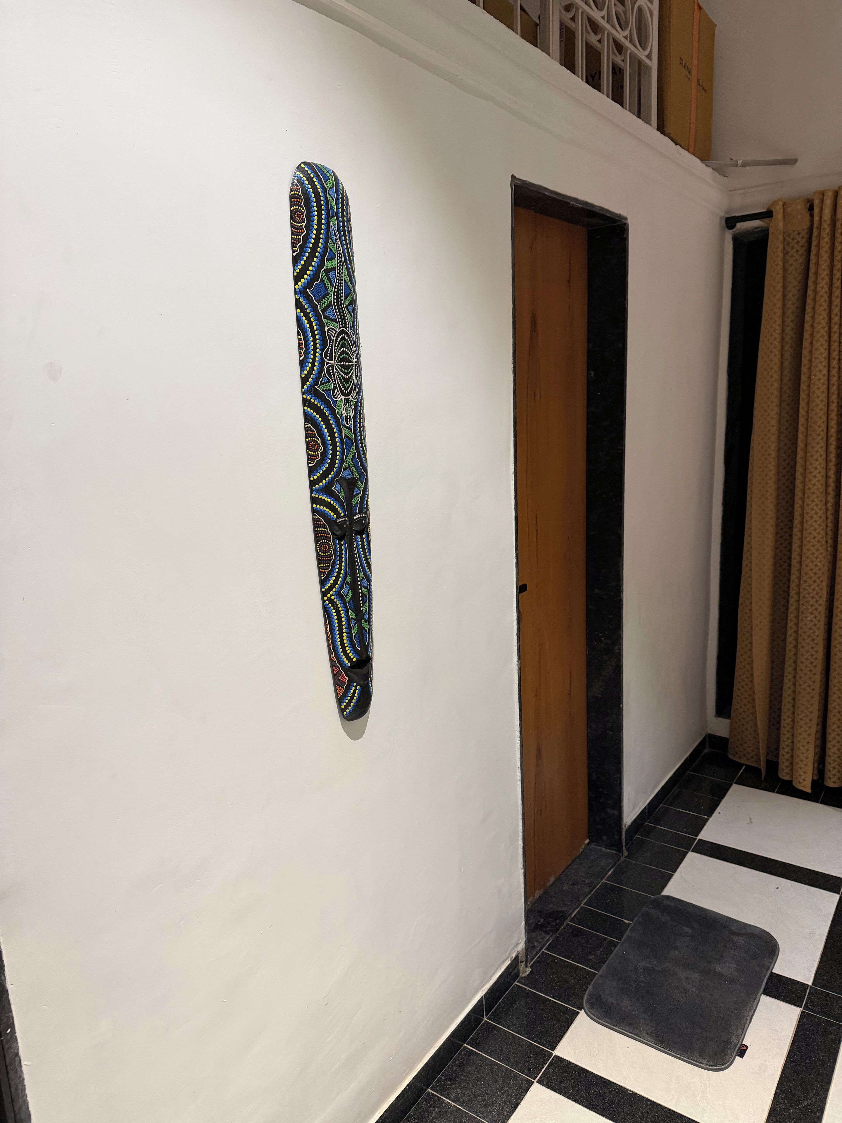 A hallway with a patterned wall decoration, a wooden door, and a checkered floor.