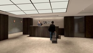 Aula, jossa on vastaanottotiski, mies seisomassa tiskillä ja henkilö, jolla on matkalaukku.