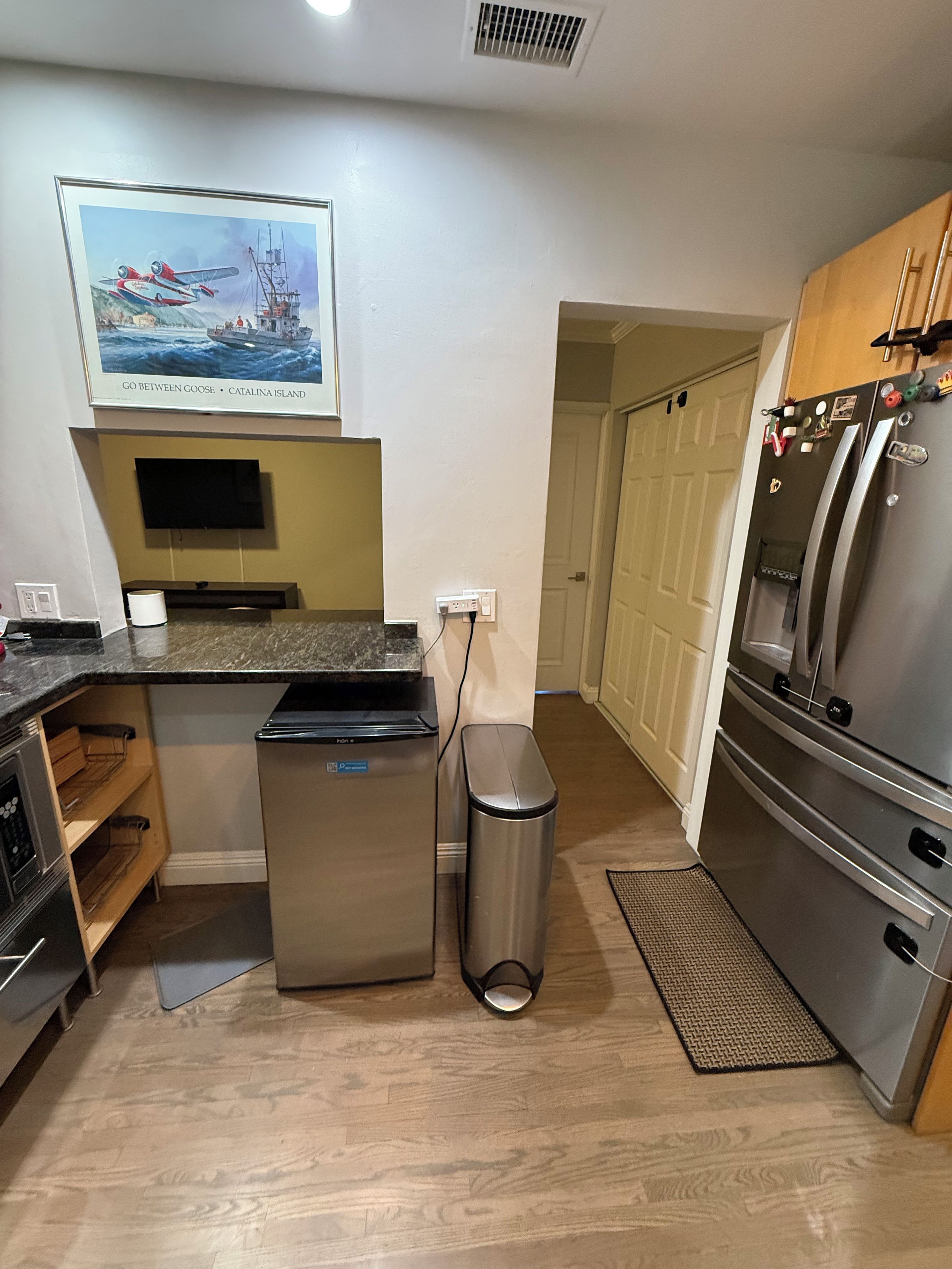 Una cocina compacta con un refrigerador de acero inoxidable, un cubo de basura y un microondas.