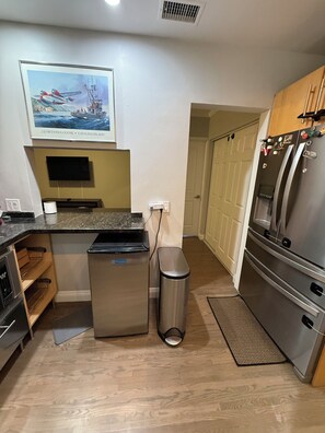 Una cocina compacta con un refrigerador de acero inoxidable, un cubo de basura y un microondas.