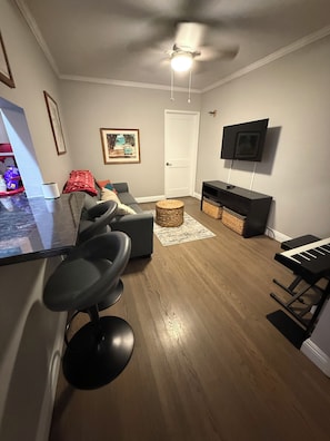 Una sala de estar moderna con una zona de bar, un televisor montado en la pared, un piano y un ventilador de techo.