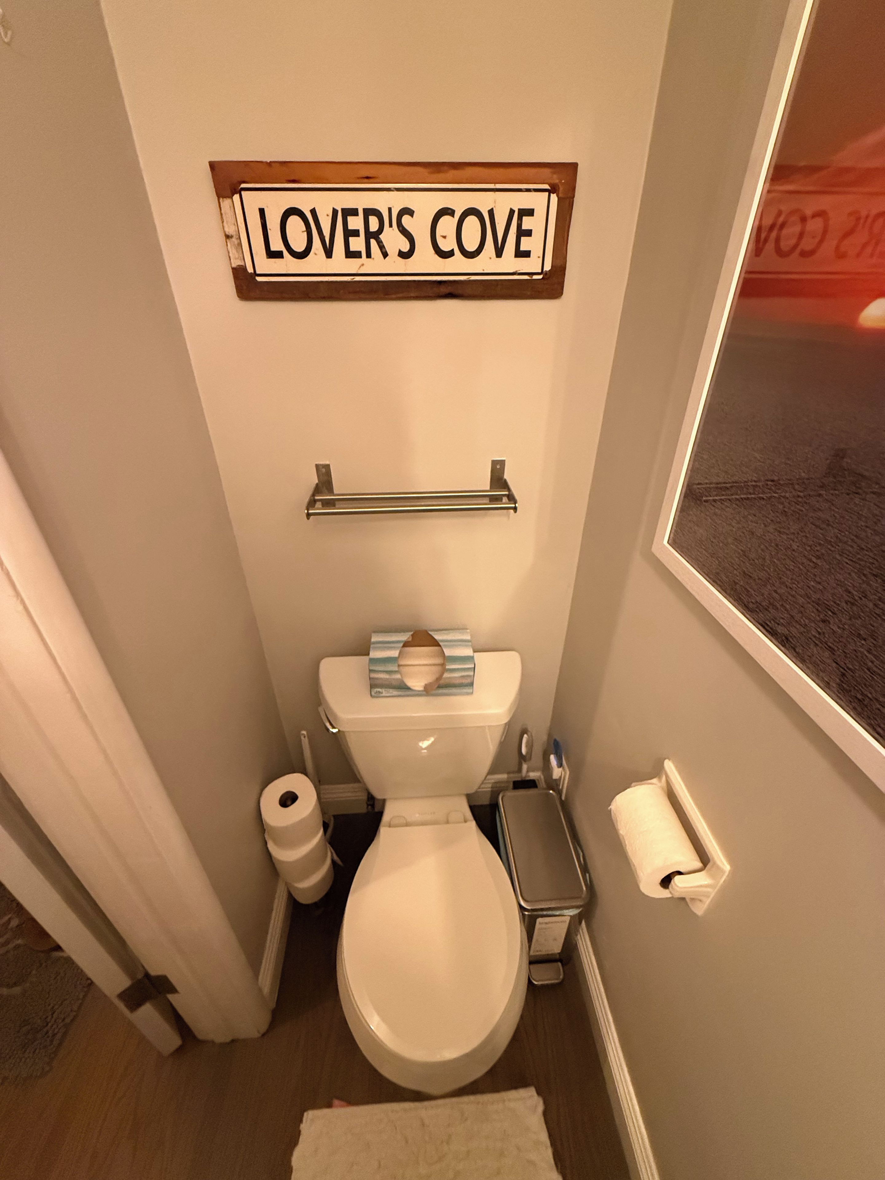 A bathroom with a toilet, a towel rack, and a sign that reads 'LOVER'S COVE'.