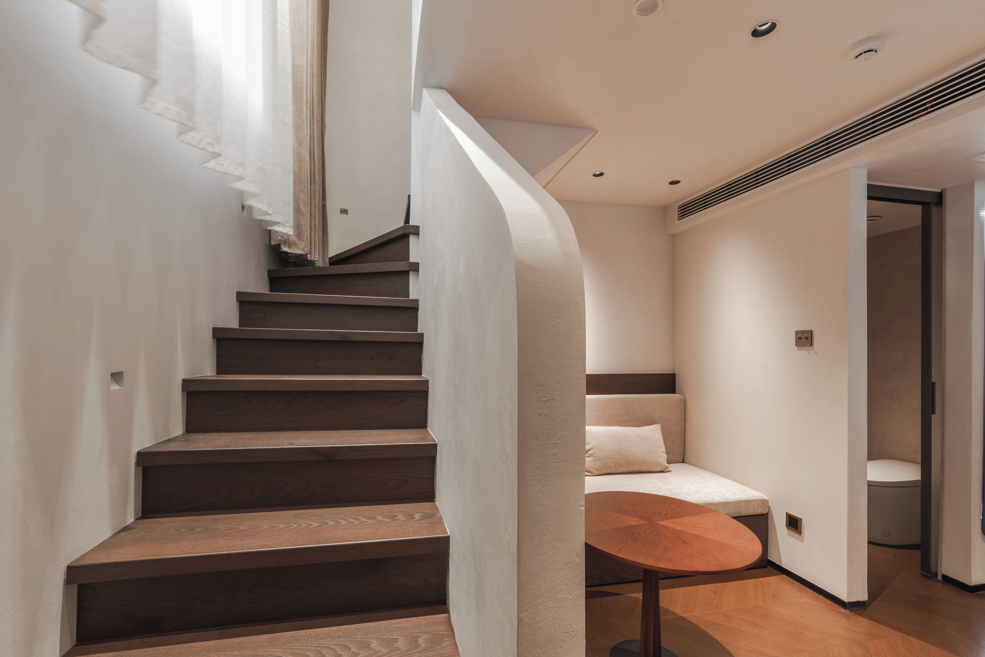 A modern interior with a wooden staircase, a round table, and a sofa.