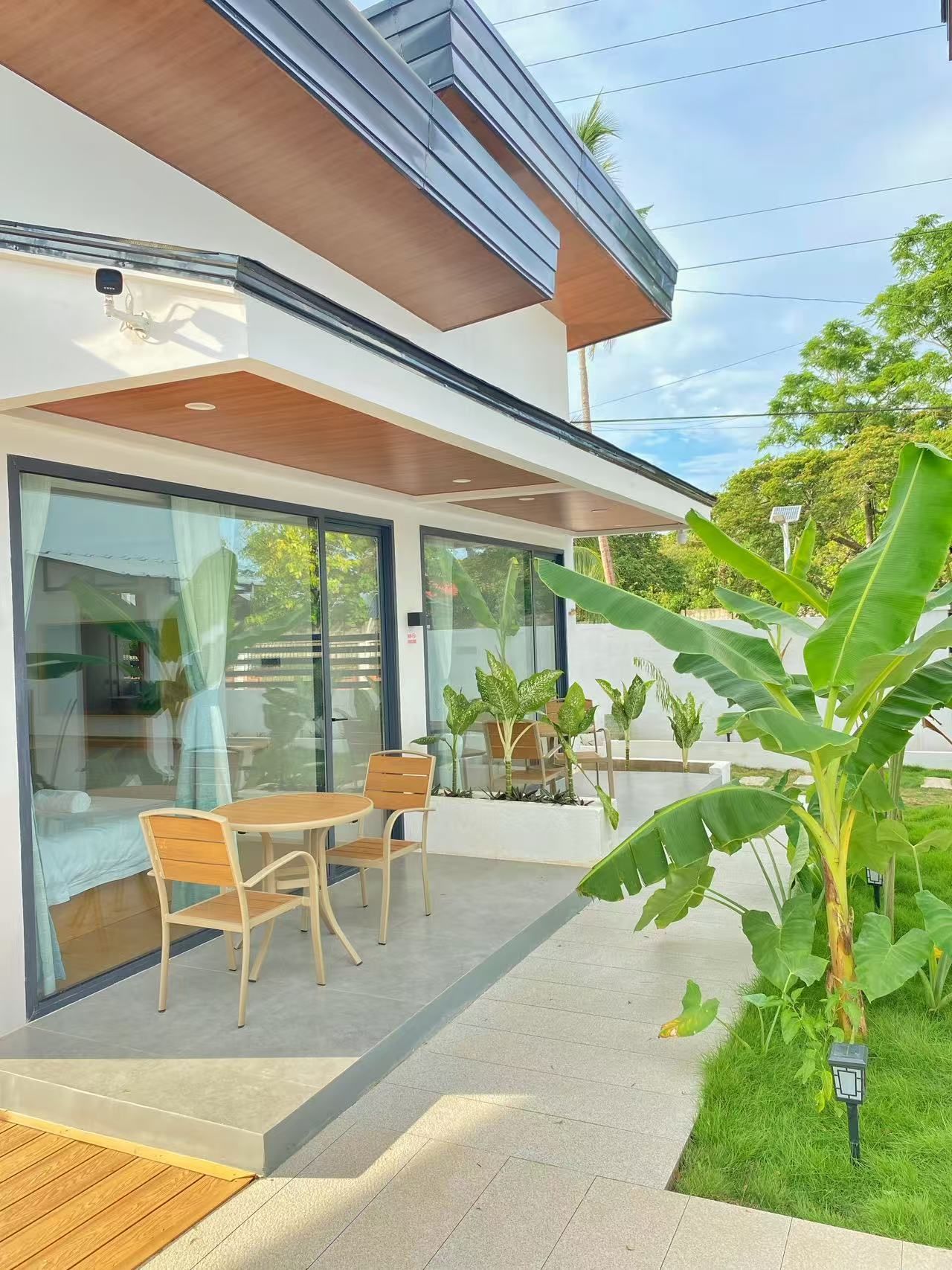 Una casa moderna con un patio, mobiliario exterior y abundante vegetación.