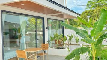 Una casa moderna con un patio, mobiliario exterior y abundante vegetación.
